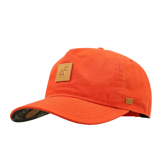 An orange cotton baseball cap with a tan leather patch on the front displaying the 'AC main' logo, shown on a plain white background.