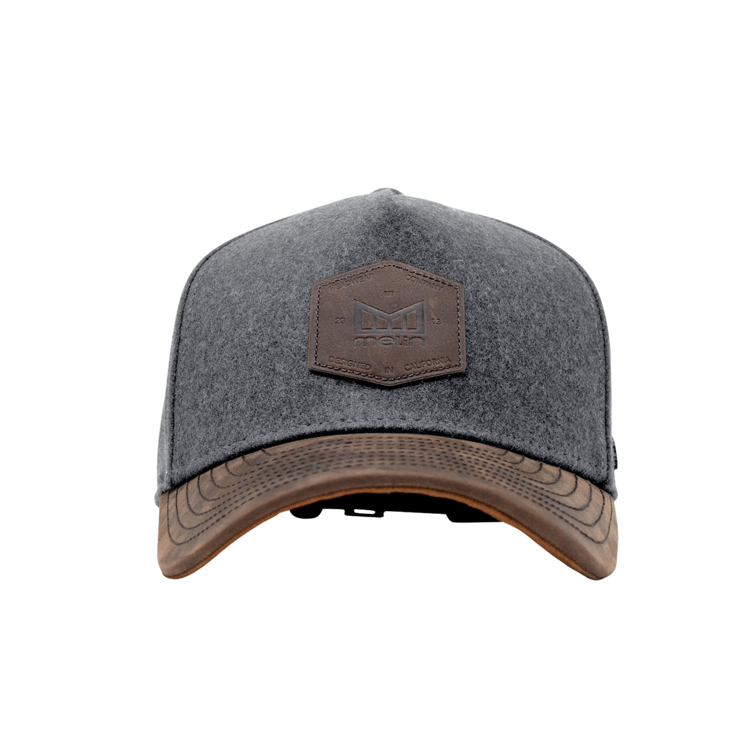 A dark gray heathered trucker-style cap with a brown leather patch on the front and a matching brown leather visor trim, shown against a plain white background.