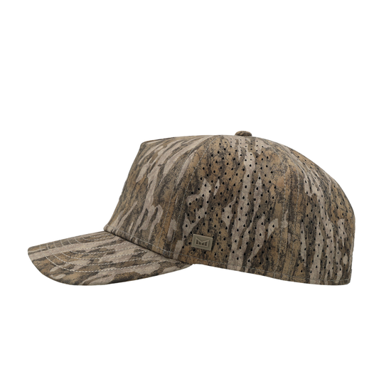 A baseball cap with a woodland camouflage pattern in shades of brown, beige, and gray, featuring a curved brim and a small rectangular logo patch on the side.