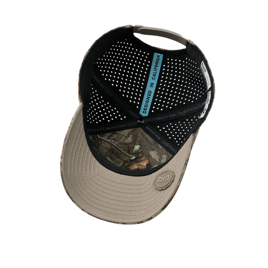 A baseball cap shown from a top-down angle on a white background, featuring a black perforated mesh back, a tan curved brim with a camouflage lens window, and a blue vertical text label on the front.