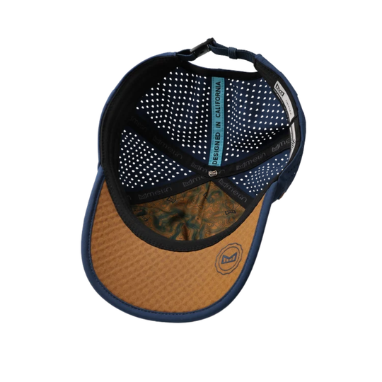 A baseball cap shown from the underside, featuring a navy blue mesh back, a tan textured brim, and a blue vertical label that reads 'DESIGNED IN CALIFORNIA'.