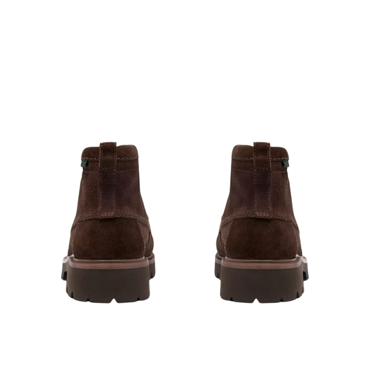 A pair of dark brown suede ankle boots shown from the back, featuring thick dark brown lug soles and a small green tag near the collar, set against a plain white background.