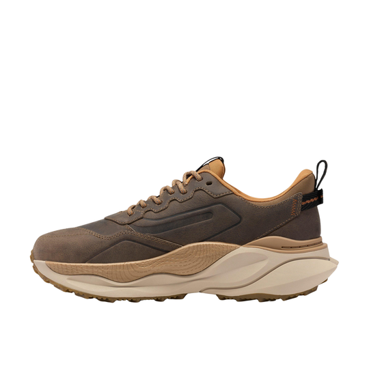 A single low-top sneaker shown in profile against a solid white background. The shoe features a dark brown suede and synthetic upper, tan midsole layers, and a thick cream-colored outsole.