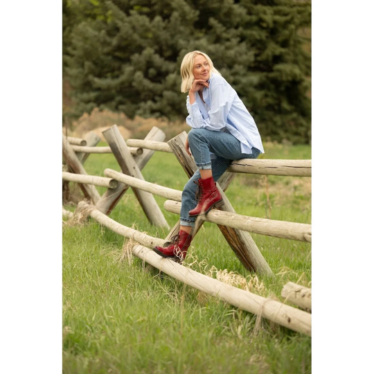 Woman sitting on a wooden fence in a grassy field with trees in the background