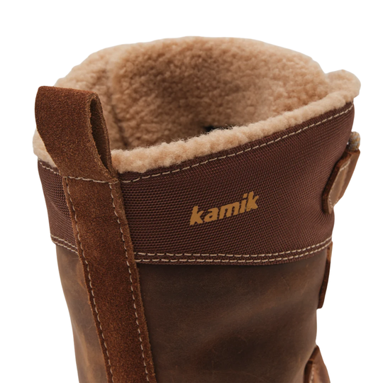 Close-up of a brown boot with a tan sherpa lining and a brown strap featuring the 'kamik' logo in gold.