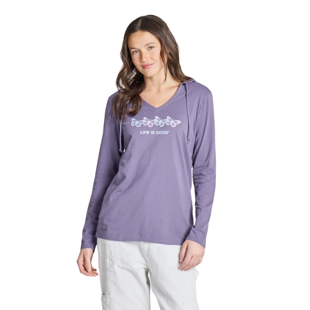 A woman modeling a lavender-purple long-sleeve V-neck hoodie with a white graphic and 'LIFE IS GOOD' text on the chest, paired with white pants against a plain white background.