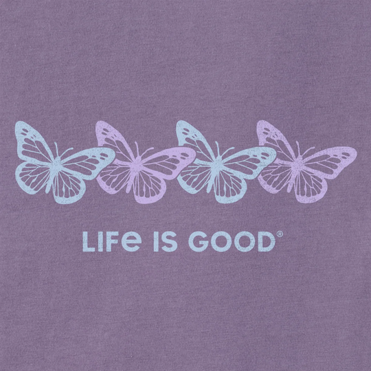 A close-up of a purple fabric surface featuring four pastel-colored butterflies in light blue, lavender, and pale purple above the text 'LIFE IS GOOD' in matching light blue lettering.