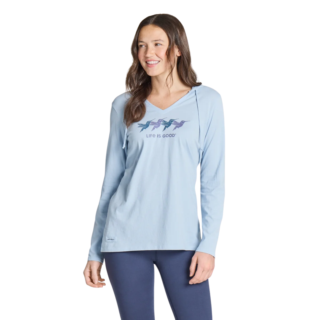 A woman modeling a light blue long-sleeve V-neck athletic top with a 'Life is Good' graphic featuring four colorful fish on the chest, paired with navy leggings, against a plain white background.