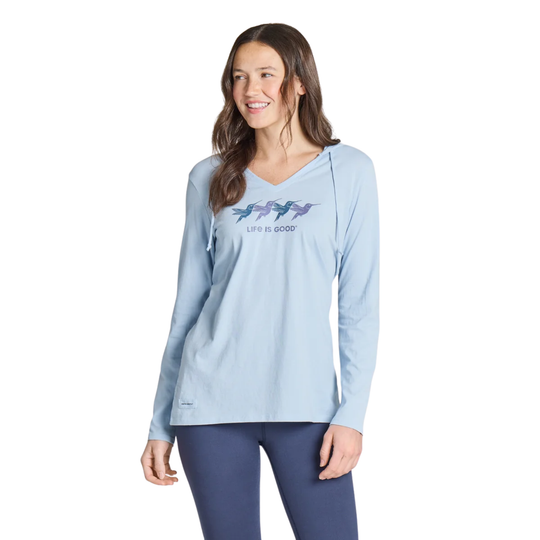 A woman modeling a light blue long-sleeve V-neck athletic top with a 'Life is Good' graphic featuring four colorful fish on the chest, paired with navy leggings, against a plain white background.