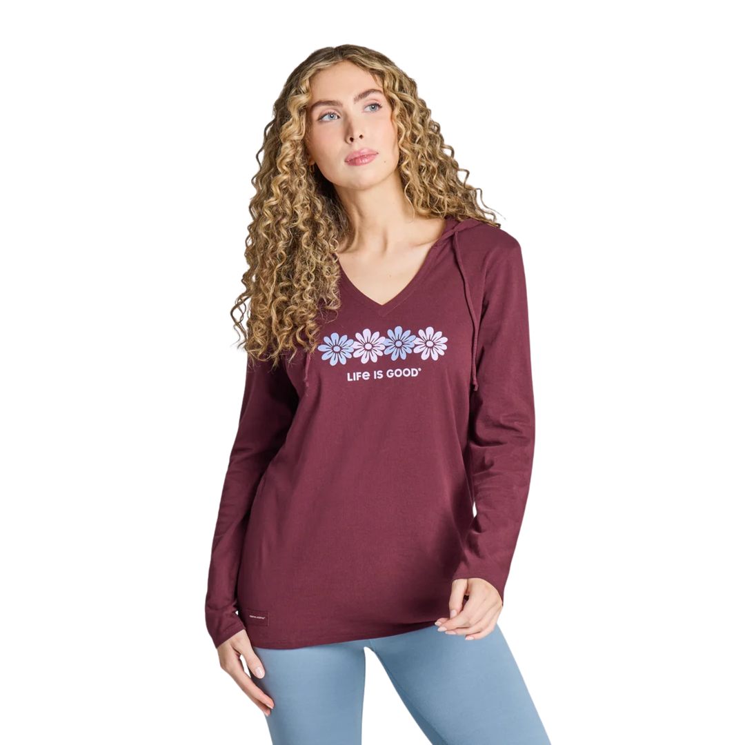 A woman with curly blonde hair wearing a maroon long-sleeve V-neck top with a white 'Life is Good' logo and a row of blue and white flowers across the chest, paired with light blue leggings, against a plain white background.