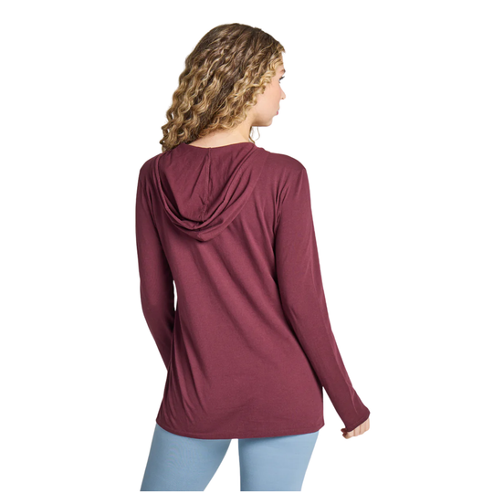 A woman with curly blonde hair is shown from the back wearing a long-sleeve maroon hooded top and light blue jeans against a plain white background.