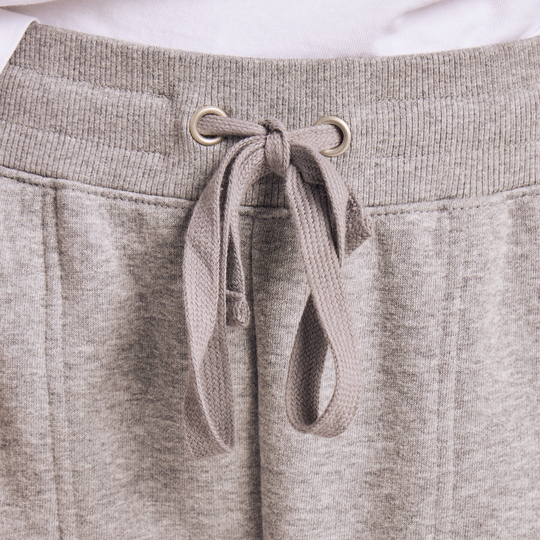Close-up of a pair of light heather gray sweatpants, focusing on the ribbed waistband, metal eyelets, and matching drawstring tie.