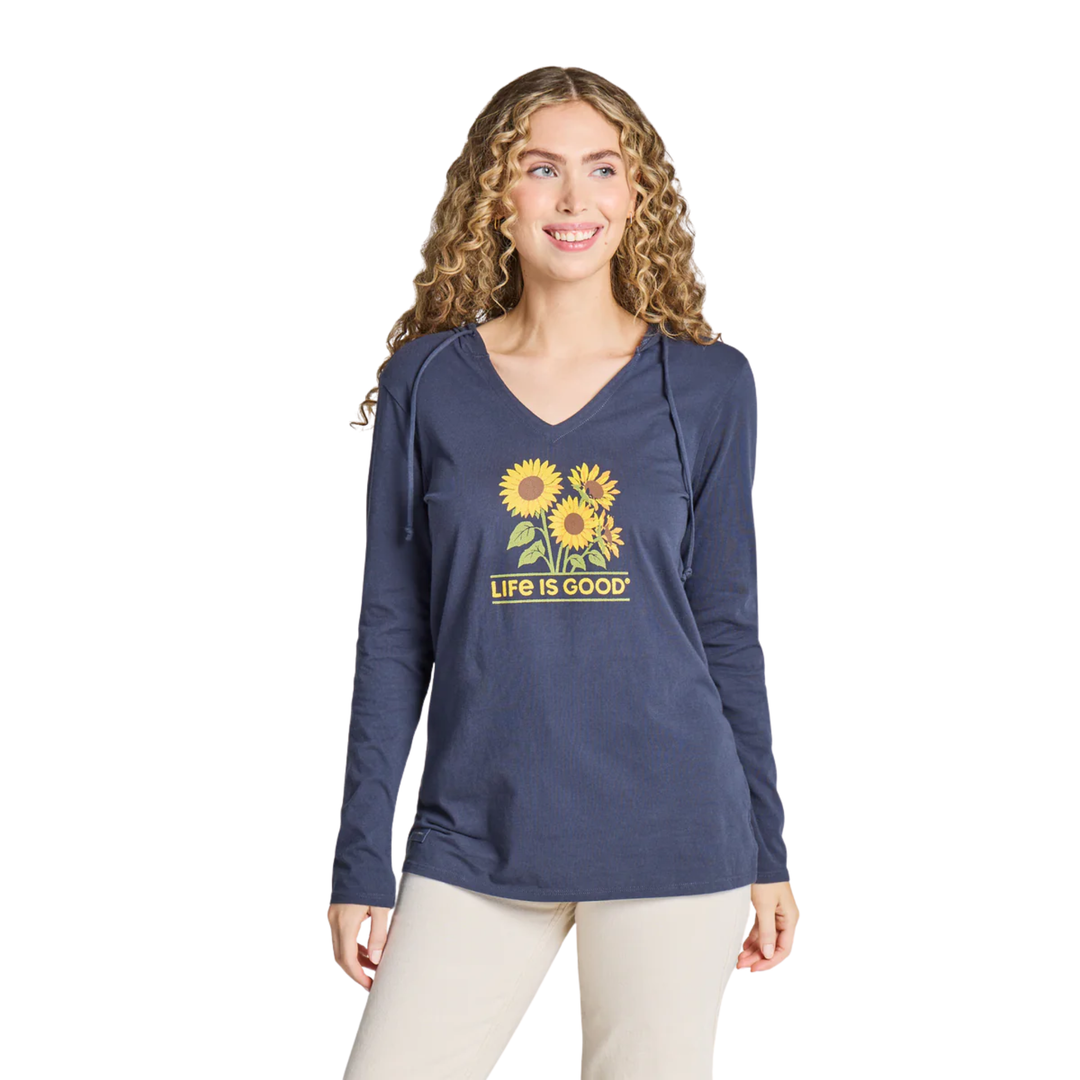A woman modeling a navy blue long-sleeve V-neck hoodie with a yellow sunflower graphic and 'LIFE IS GOOD' text on the front, paired with light beige pants, against a plain white background.