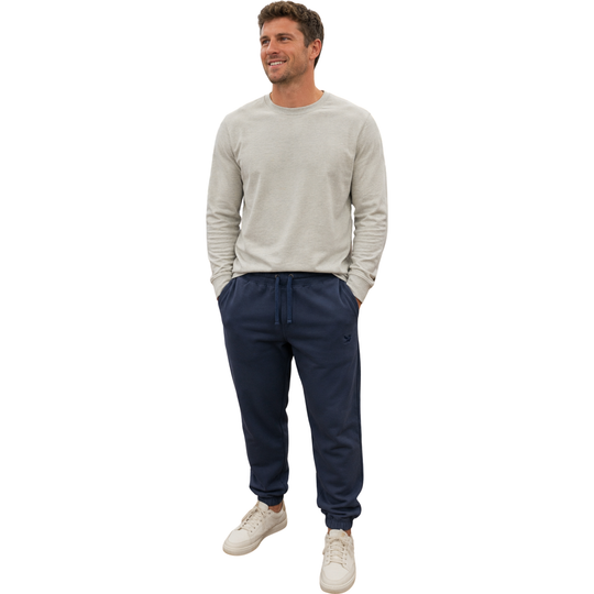 A man modeling a light gray long-sleeve crewneck sweater and navy blue jogger sweatpants with white sneakers, set against a plain white background.
