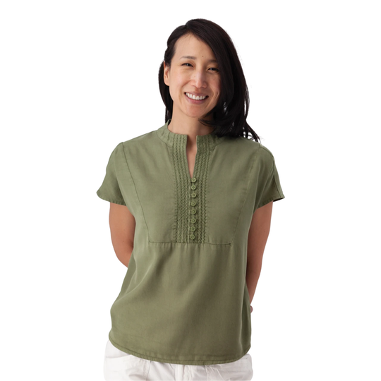 A woman wearing a short-sleeve olive green blouse with a split neckline, decorative button placket, and embroidered chest detailing, paired with white pants, against a plain white background.