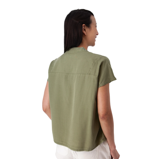 A woman shown from the back wearing a short-sleeve sage green shirt and white pants against a plain white background.