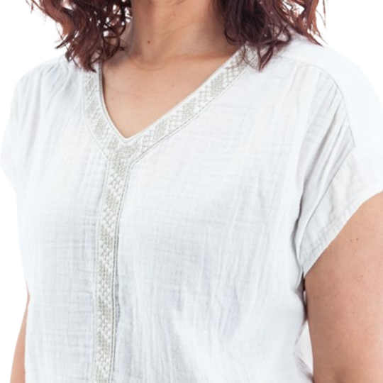 A close-up of a woman wearing a white short-sleeve V-neck top with light beige embroidered trim along the neckline and center front placket.