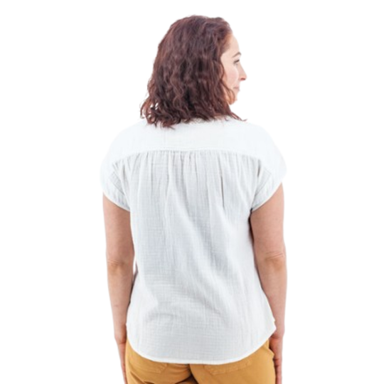 A woman viewed from the back wearing a white short-sleeve textured blouse and mustard yellow pants, set against a plain white background.
