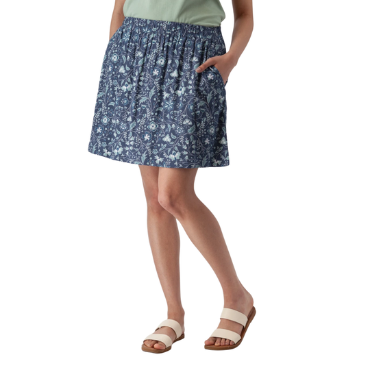 A model wearing a blue and white floral print skirt with side pockets, paired with a sage green top and beige double-strap sandals, shown against a plain white background.