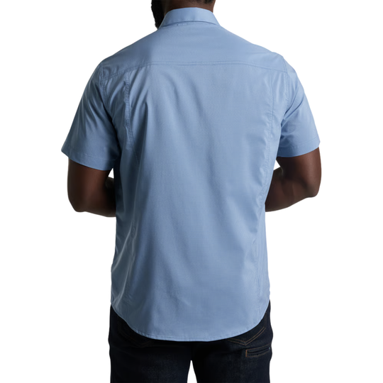 A man viewed from the back wearing a light blue short-sleeve button-up shirt and dark jeans against a plain white background.