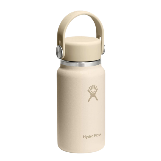 A Hydro Flask insulated water bottle in a light beige color, featuring a matching beige lid with a built-in carrying loop and a silver metal band near the top.