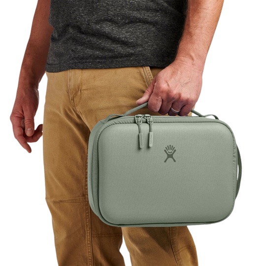 Person holding a green travel case with a brand logo on a white background
