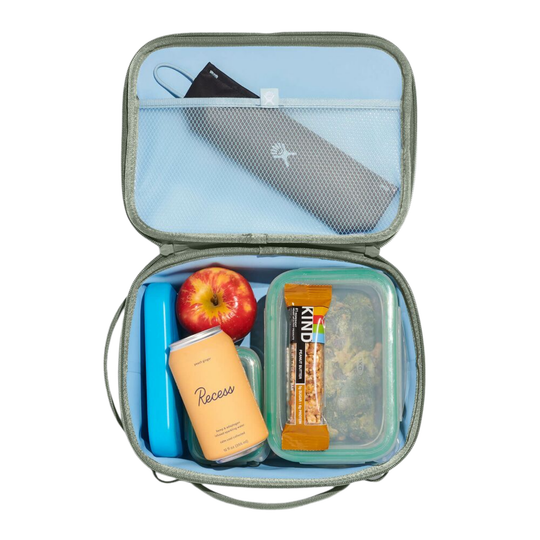 An open gray lunch bag with a light blue interior, shown from above on a white background. Inside are a black face mask in the mesh pocket, a blue lunchbox, an apple, a can of Reese's, and a clear container holding a granola bar.
