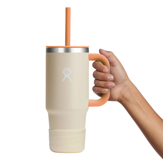 A hand holding a large insulated tumbler with a handle, straw, and a visible Hydro Flask logo on the front, against a plain white background.