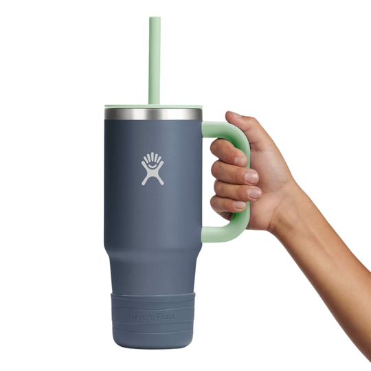 Hand holding a blue mug with a green handle and straw on a white background