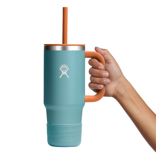Hand holding a teal mug with an orange handle and straw on a white background