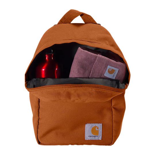 An open brown Carhartt backpack shown against a white background, with a red bottle and a folded pink Carhartt towel visible inside.