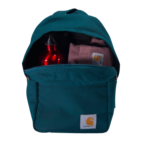 A teal Carhartt backpack shown open, revealing a red bottle and a folded dusty pink Carhartt towel inside. The front pocket features a white Carhartt logo patch.