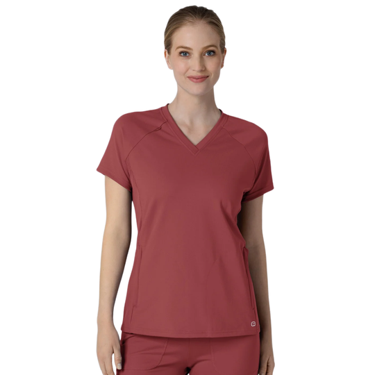 A woman modeling a short-sleeve V-neck scrub top in a muted brick red color, paired with matching scrub pants, against a plain white background.