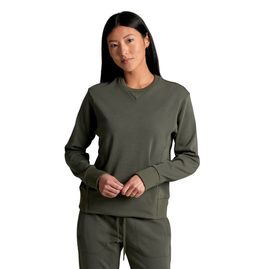 A woman modeling an olive green crewneck sweatshirt and matching sweatpants against a solid white background.