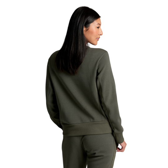 A woman with long black hair is shown from the back wearing an olive green crewneck sweatshirt and matching sweatpants against a solid white background.