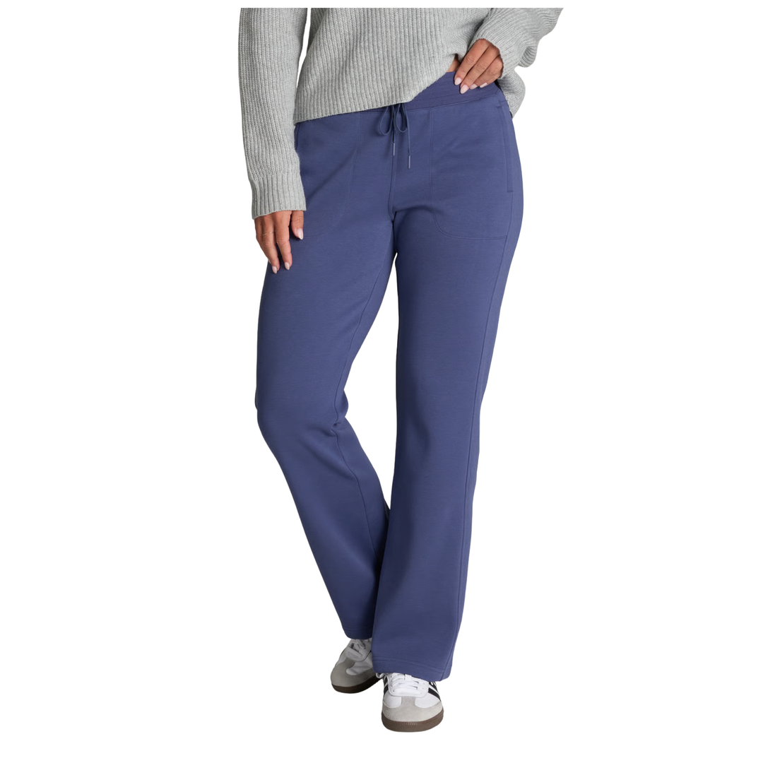 A model wearing a pair of slate blue scrub pants with a drawstring waist, paired with a gray ribbed sweater and gray sneakers, shown from the waist down on a white background.