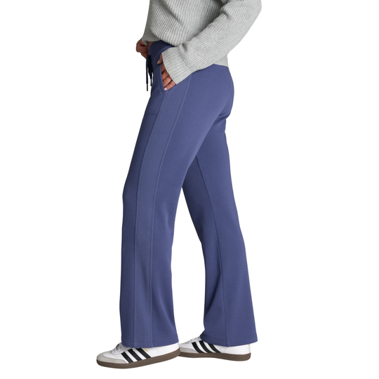 A person shown from the waist down wearing blue wide-leg scrub pants, a gray ribbed sweater, and white Adidas sneakers with black stripes, set against a plain white background.