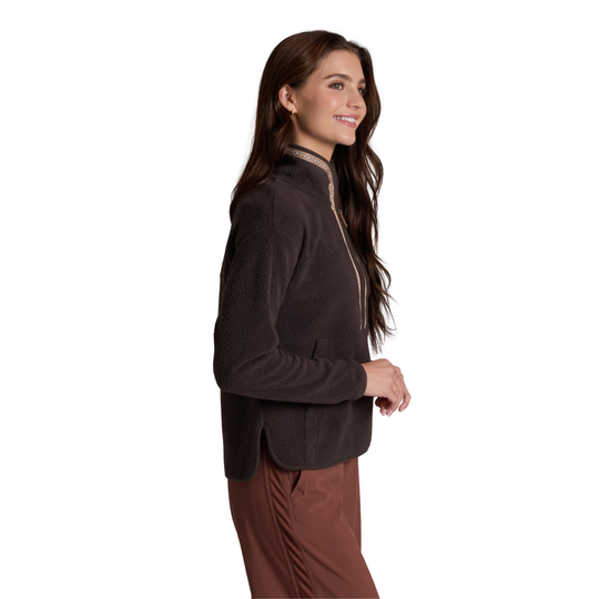 A woman wearing a dark brown fleece pullover jacket with a high mock neck and a subtle textured pattern, paired with brown pants, shown from a side profile against a solid white background.