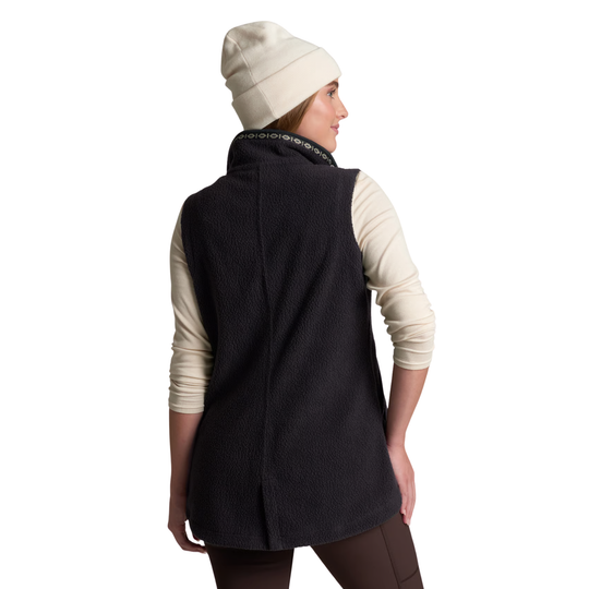 A woman shown from the back wearing a dark charcoal fleece vest over a cream long-sleeve shirt, a cream knit beanie, and brown leggings, against a plain white background.