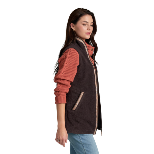 A woman wearing a dark brown fleece vest with a rust-colored ribbed knit sweater underneath, paired with blue jeans, shown from a side profile against a white background.