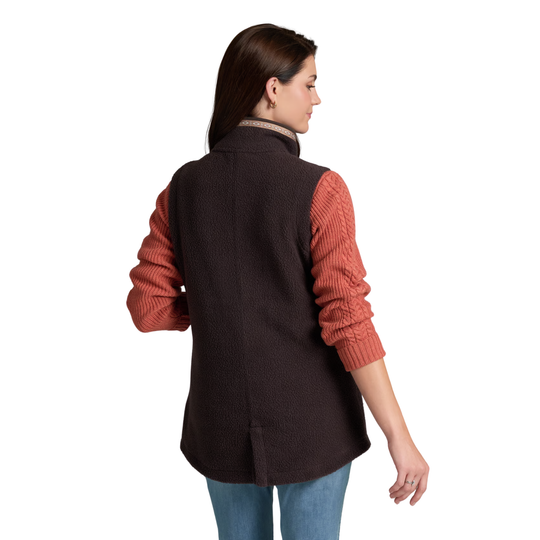 A woman shown from the back wearing a dark brown vest over a rust-orange cable-knit sweater, paired with blue jeans, against a plain white background.