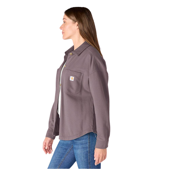 A woman modeling a Carhartt long-sleeve button-up work shirt in a dusty purple color, paired with blue jeans, against a plain white background.