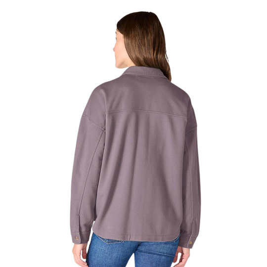 A woman viewed from the back wearing a muted mauve-gray button-up shirt jacket with blue jeans, set against a plain white background.