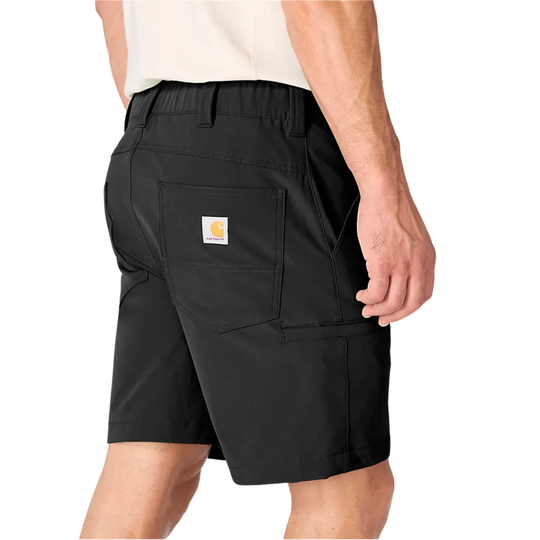 Rear three-quarter view of a person wearing black Carhartt work shorts with a white shirt partially visible, on a light gray studio background.