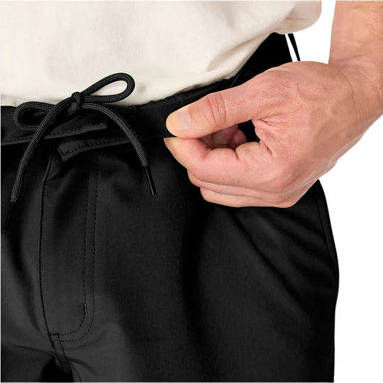 Close-up of a person wearing black drawstring pants, with one hand adjusting the waistband.