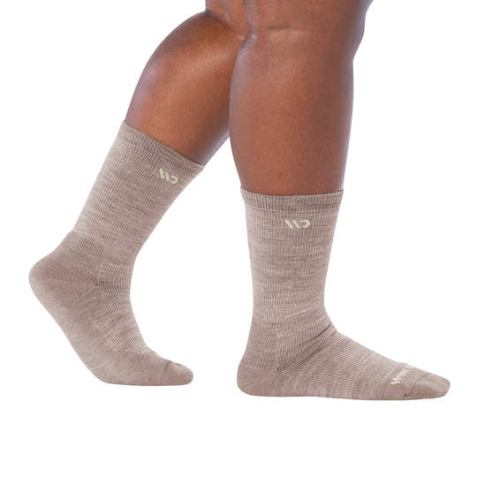 A pair of crew-length athletic socks in a heathered taupe-beige color, shown on a person's legs against a plain white background.