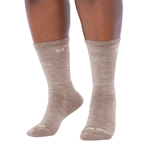 A pair of crew-length athletic socks in a heathered taupe-beige color, shown on a person's legs against a plain white background.