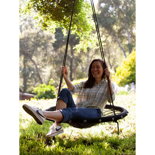 Old Ranch Women's Reagan Pull On Crop Pant - Vintage Indigo on a female model sitting on a swing with green grass and foliage behind her. 