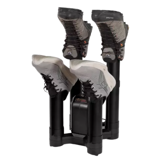 A pair of hiking boots placed on a black dual-station boot dryer with a battery pack, isolated on a white background.