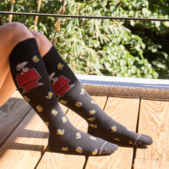 Black socks with cartoon character design worn by a person on a wooden deck.